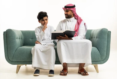 Saudi Father and Son Reading Book on Sofa