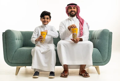 Saudi Father and Son Eating Popcorn on Green Sofa Studio