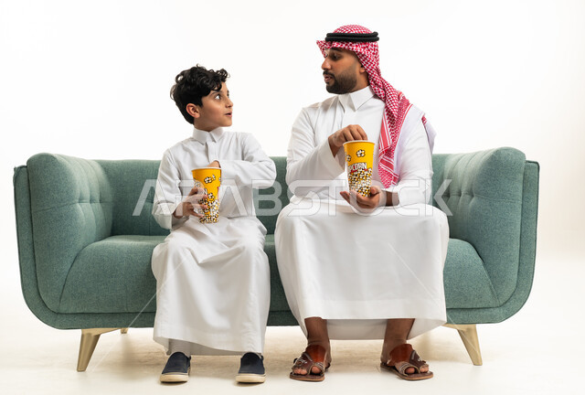 أب سعودي وابنه يتناولان الفشار على الأريكة