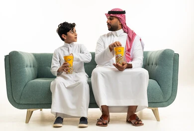 Saudi Father and Son Eating Popcorn on Sofa