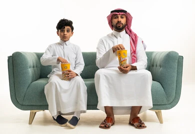Surprised Saudi Man and Boy Eating Popcorn on Sofa