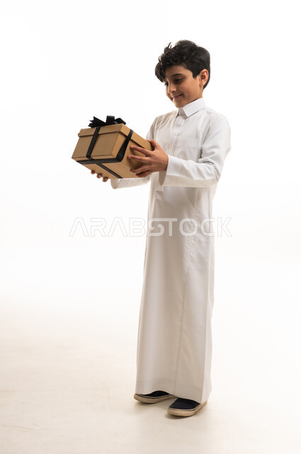 طفل سعودي بالثوب التقليدي يمسك صندوق هدايا