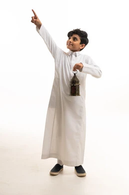 طفل سعودي بالثوب الأبيض يمسك فانوساً ويشير للأعلى
