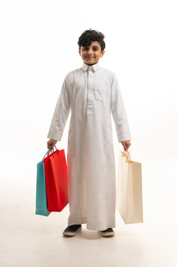 طفل سعودي بالثوب التقليدي يحمل أكياس تسوق ملونة