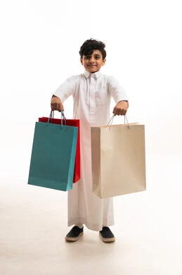طفل سعودي بالثوب التقليدي يحمل حقائب تسوق ملونة