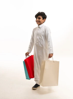طفل سعودي بالثوب التقليدي يحمل حقائب تسوق