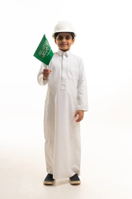 طفل سعودي بالثوب والخوذة يحمل العلم السعودي