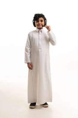 طفل سعودي بالثوب التقليدي يرتدي سماعة رأس بخلفية بيضاء