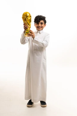 طفل سعودي بالثوب يحمل مجسم كأس العالم الذهبي