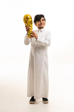 طفل سعودي بالثوب التقليدي يحمل كأساً ذهبياً