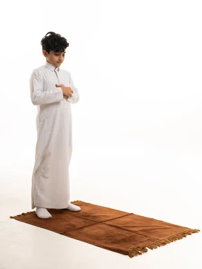 طفل سعودي بالثوب الأبيض يصلي على السجادة
