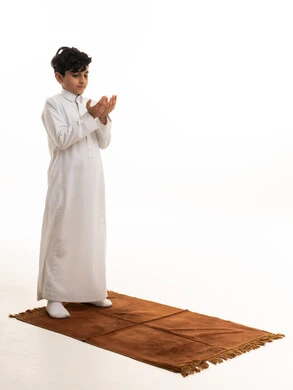طفل سعودي بالثوب الأبيض يصلي على السجادة