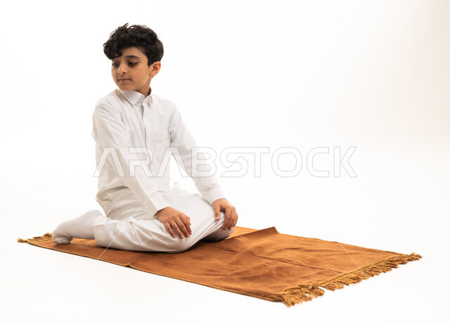 طفل سعودي بالثوب التقليدي يصلي على السجادة