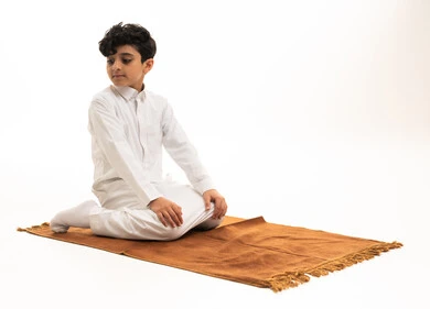 طفل سعودي بالثوب التقليدي يصلي على السجادة