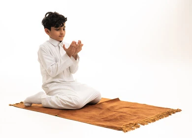 Saudi Arabian Boy in White Thobe Praying on Mat