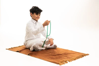 طفل سعودي بالثوب الأبيض يحمل مسبحة خضراء