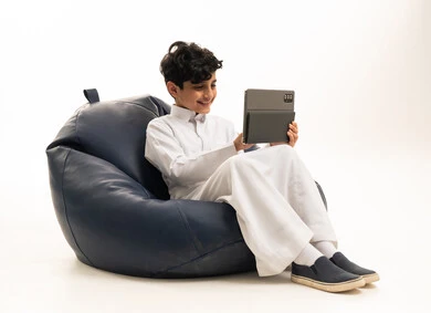 طفل سعودي يستخدم جهاز لوحي على كرسي بين باج