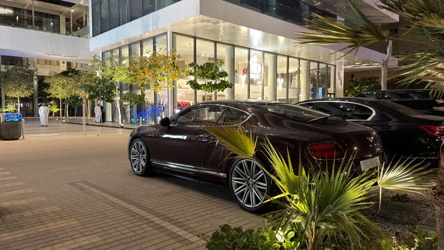 سيارة فاخرة متوقفة أمام مجمع تجاري حديث في الليل