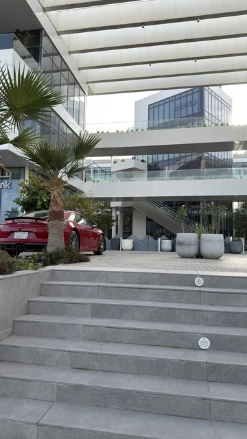 سيارة حمراء فاخرة أمام مجمع تجاري حديث بالرياض