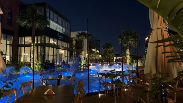 مطعم خارجي مع نوافير مضيئة باللون الأزرق ليلاً