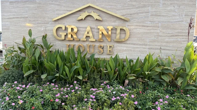 لوحة جراند هاوس الخارجية على جدار حجري مع حديقة