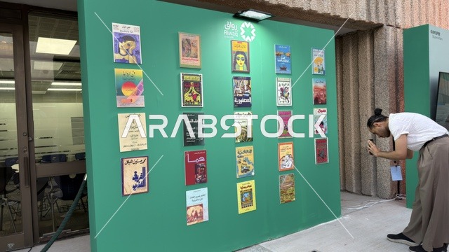 رجل يصور أغلفة كتب عربية على جدار عرض أخضر في معرض ثقافي