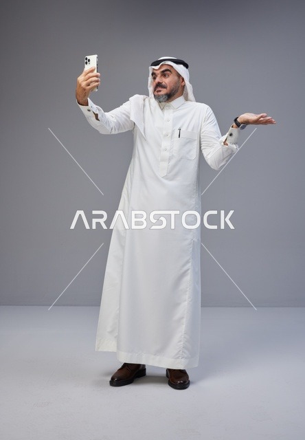 رجل سعودي بالزي التقليدي يلتقط صورة سيلفي في الاستوديو