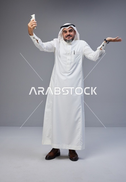 رجل سعودي بالزي التقليدي يلتقط صورة سيلفي في الاستوديو