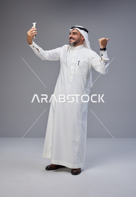 رجل سعودي بالزي التقليدي يلتقط صورة سيلفي في الاستوديو