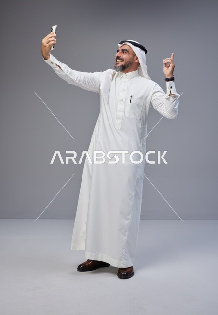 رجل سعودي بالزي التقليدي يلتقط سيلفي بالهاتف الذكي