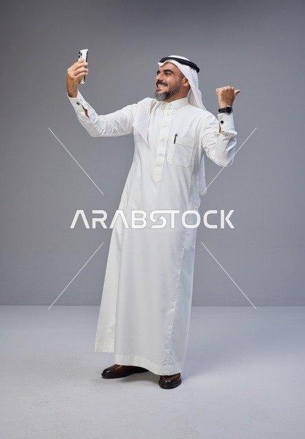 رجل سعودي بالزي التقليدي يلتقط صورة سيلفي بالجوال
