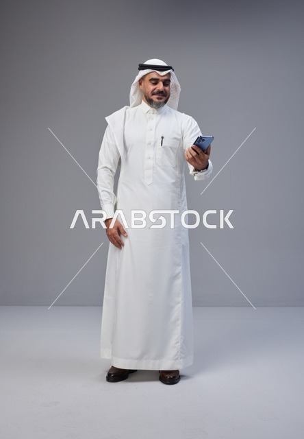 رجل سعودي بالزي التقليدي يستخدم الهاتف الذكي في الاستوديو