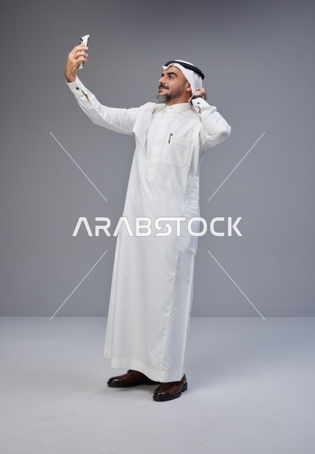 رجل سعودي بالزي التقليدي يلتقط سيلفي بالهاتف الذكي
