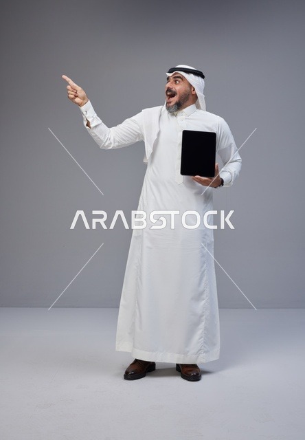 Saudi Man with Tablet Pointing Upward on Grey Background