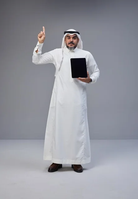 Saudi Man Holding Tablet Pointing Up on Grey Background