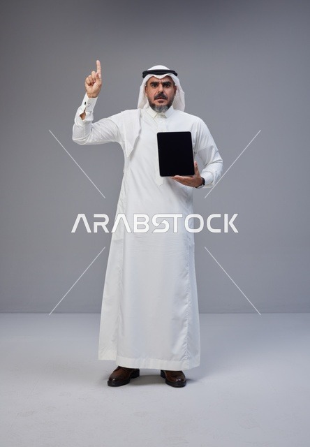 رجل سعودي يحمل جهاز لوحي ويشير للأعلى