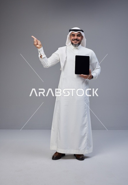 Saudi Man Holding Blank Tablet Pointing Upwards in Studio