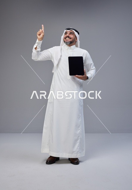 Saudi Man Holding Tablet and Pointing Up in Studio