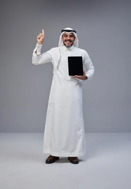 Saudi Man Holding Tablet Pointing Up on Grey Background