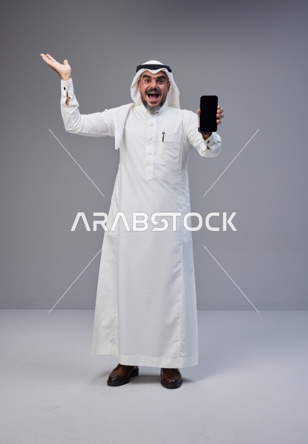 رجل سعودي يحمل هاتف بشاشة فارغة خلفية رمادية