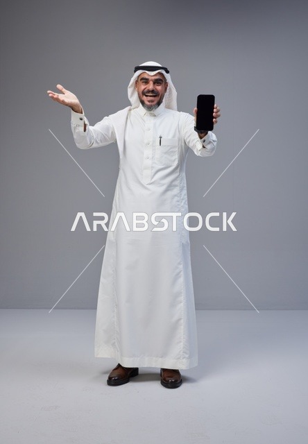 رجل سعودي يحمل هاتفاً ذكياً بشاشة فارغة