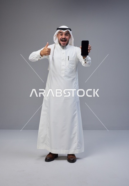رجل سعودي مع هاتف ذكي بشاشة فارغة وإشارة الإبهام