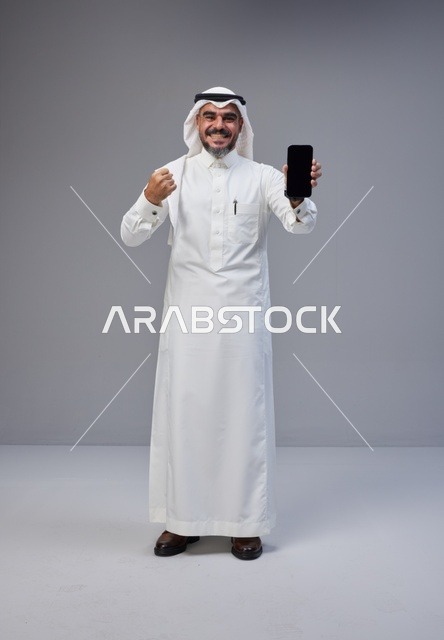 رجل سعودي بالزي التقليدي يحمل هاتفاً بشاشة فارغة
