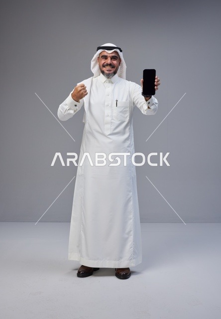 رجل سعودي بالزي التقليدي يحمل هاتف بشاشة فارغة