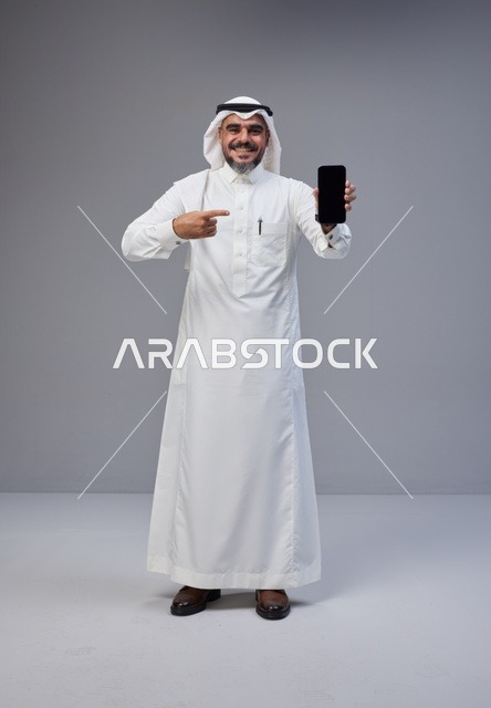 رجل سعودي بالزي التقليدي يحمل هاتف بشاشة فارغة