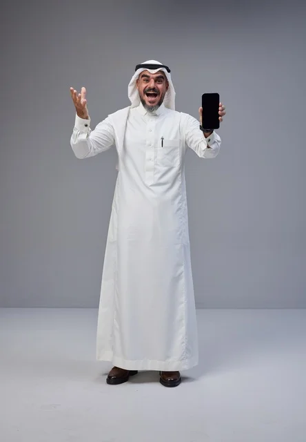 رجل سعودي بالزي التقليدي يحمل هاتفاً بشاشة فارغة