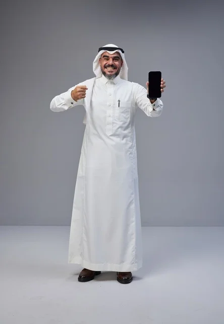 رجل سعودي بالزي التقليدي يحمل هاتفاً ذكياً بشاشة فارغة