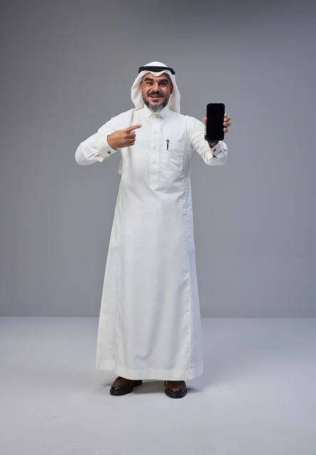 رجل سعودي بالزي التقليدي يشير إلى هاتف ذكي