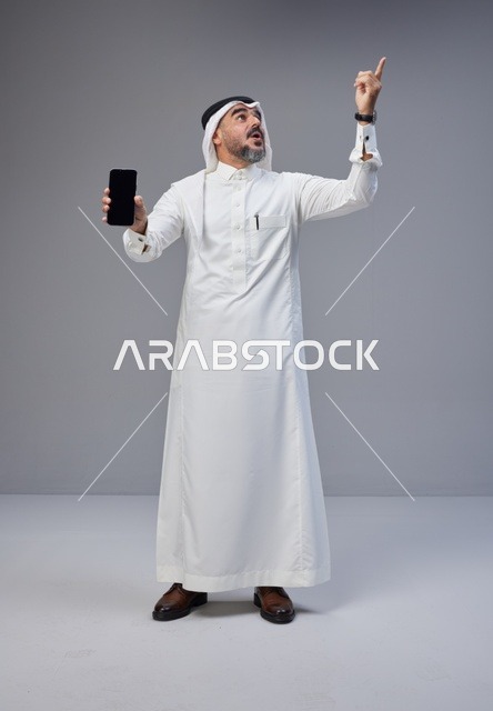 رجل سعودي يحمل هاتف بشاشة فارغة ويشير للأعلى