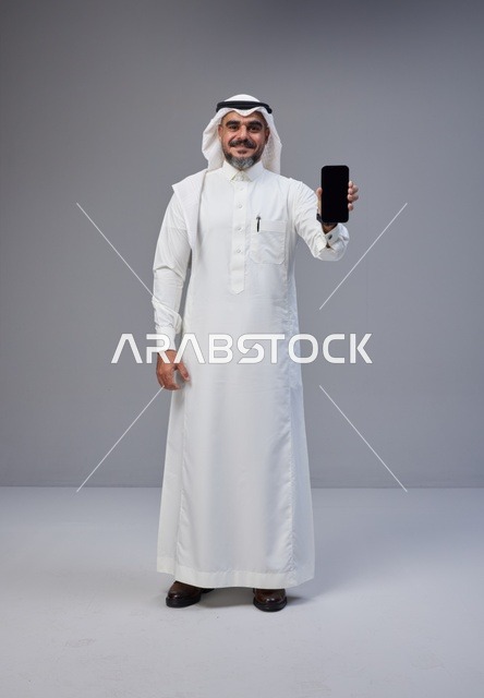 رجل سعودي بالزي التقليدي يحمل هاتفاً بشاشة فارغة